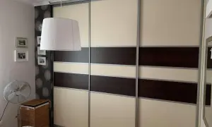Oklejanie szafy przesuwnej w beżowo-brązowe pasy. W tle widać lampę, zdjęcia i wentylator.
