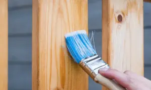 Pędzel z niebieskim włosiem nakłada bezbarwny impregnat na drewniane balustrady. Dowiedz się, czym zabezpieczyć drewno na zewnątrz, by służyło latami.