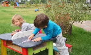 Dzieci tworzą cuda z palet, rysując kredą na stoliku.