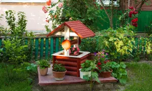 Uroczy, drewniany domek studni z ozdobnymi detalami, otoczony kwitnącymi roślinami. Ciekawe ozdoby z drewna do ogrodu dodają mu charakteru.