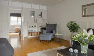 Jasny salon z pomalowaną boazerią, szarym fotelem i kanapą, książkami i wiklinowymi koszami.