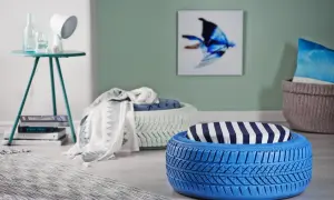 Niebieskie i białe pufy z opon do ogrodu, ozdobione poduszkami i kocami, tworzą przytulny kącik.