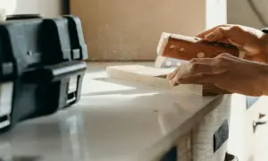 Ręce szlifują drewno, tworząc pył. Precyzyjne szlifowanie forniru to klucz do pięknego wykończenia.