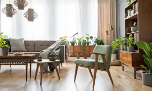 Wnętrze z meblami po renowacji PRL: sofa, fotele, stoliki i regał w stylu retro, ozdobione licznymi roślinami.