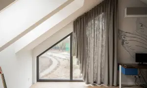 Eleganckie karnisze na skośne okna idealnie komponują się z szarymi zasłonami, tworząc przytulną atmosferę w pokoju na poddaszu.