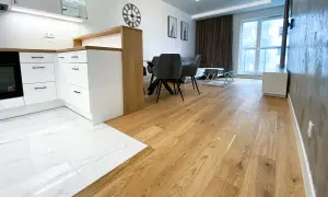 Eleganckie łączenie podłogi drewnianej z płytkami w nowoczesnym wnętrzu. Drewniana podłoga płynnie przechodzi w białe płytki z marmurowym wzorem.