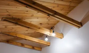 Drewniany sufit z belkami, tworzący przytulną atmosferę. Dwie lampy wiszące oświetlają przestrzeń.