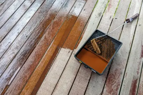 Malowanie boazerii na tarasie. Drewniane deski odzyskują blask dzięki brązowej lazurze.