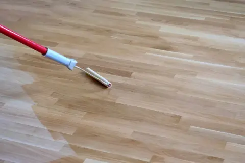 Wałek do malowania starej podłogi drewnianej nakłada nową warstwę ochronną, odnawiając jej wygląd.