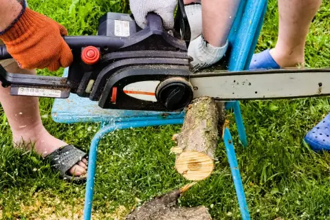 Osoba w pomarańczowej rękawicy używa piły łańcuchowej do cięcia drewna na prowizorycznym stojaku. To prosty sposób, jak zrobić stojak do cięcia drewna.