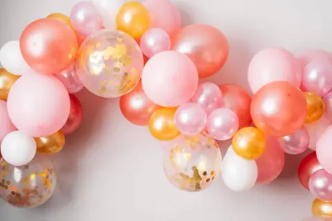 Ładna girlanda z balonów w odcieniach różu, brzoskwini i złota. Zobacz, jak zamocować balony na taśmie, by stworzyć efektowną dekorację.