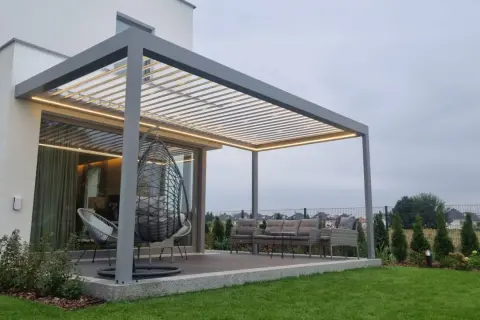 Nowoczesna pergola z oświetleniem LED. Zastanawiasz się, czym pomalować pergole? Ta szara konstrukcja świetnie komponuje się z meblami ogrodowymi i zielenią.