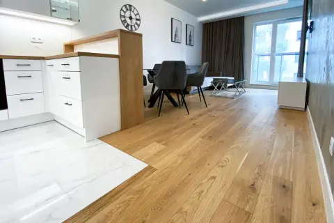 Eleganckie łączenie podłogi drewnianej z płytkami w nowoczesnym wnętrzu. Drewniana podłoga płynnie przechodzi w białe płytki z marmurowym wzorem.