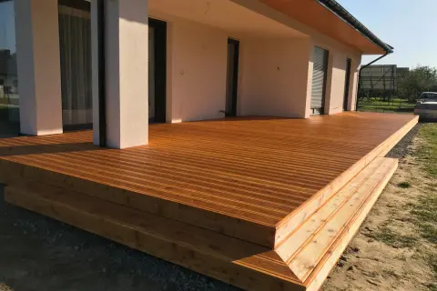 Nowa, drewniana terasa z widocznymi stopniami, zabezpieczona impregnatem do legarów tarasowych, lśni w słońcu.