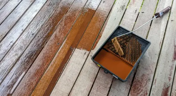 Malowanie boazerii na tarasie. Drewniane deski odzyskują blask dzięki brązowej lazurze.