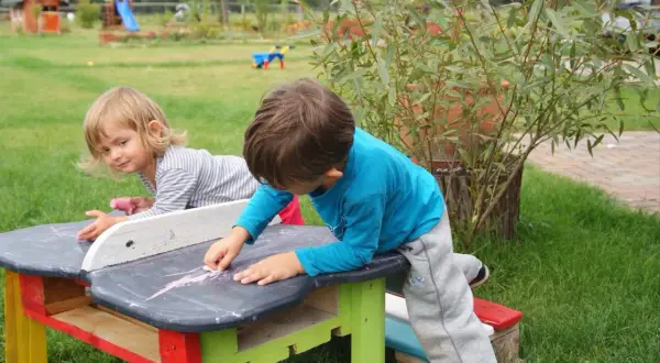 Dzieci tworzą cuda z palet, rysując kredą na stoliku.