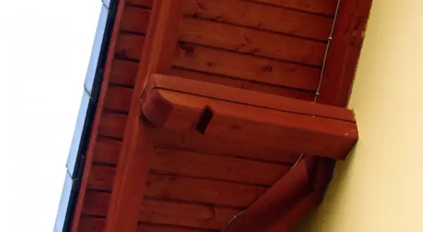 Drewniana podbitka dachu, świeżo po malowaniu, z widocznymi elementami konstrukcyjnymi i fragmentem żółtej ściany.