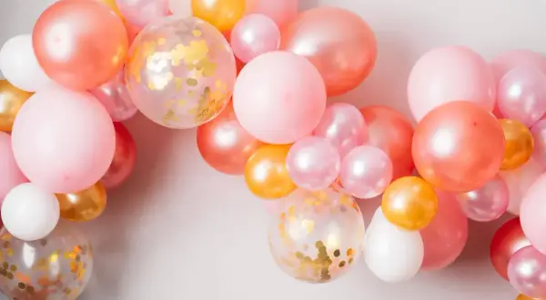 Ładna girlanda z balonów w odcieniach różu, brzoskwini i złota. Zobacz, jak zamocować balony na taśmie, by stworzyć efektowną dekorację.