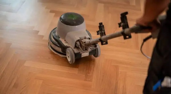 Samodzielne cyklinowanie parkietu. Maszyna szlifuje drewnianą podłogę w jodełkę, przywracając jej blask.