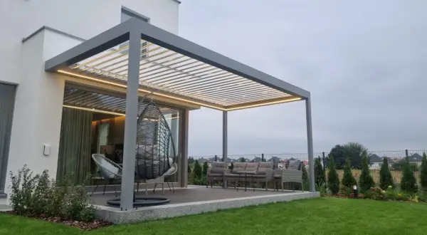 Nowoczesna pergola z oświetleniem LED. Zastanawiasz się, czym pomalować pergole? Ta szara konstrukcja świetnie komponuje się z meblami ogrodowymi i zielenią.