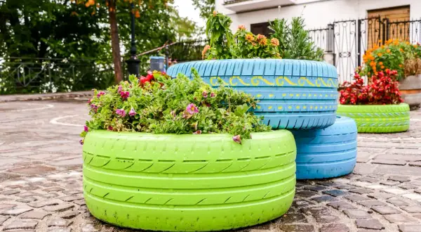 Kolorowe dekoracje z opon do ogrodu, wypełnione kwitnącymi roślinami, tworzą radosną kompozycję na brukowanym placu.