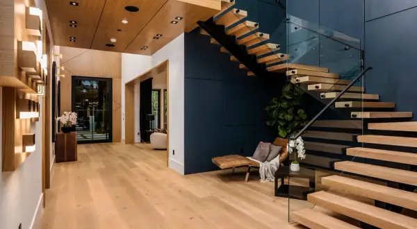 Nowoczesne wnętrze z dominującymi naturalnymi **kolorami drewna** na podłodze i schodach, kontrastujące z granatową ścianą.