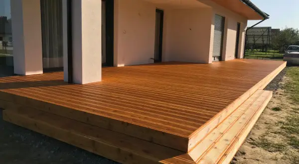 Nowa, drewniana terasa z widocznymi stopniami, zabezpieczona impregnatem do legarów tarasowych, lśni w słońcu.