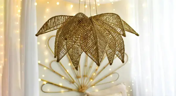 Złota lampa z koralików diy w kształcie liścia, wisząca na tle białych zasłon i migoczących światełek.