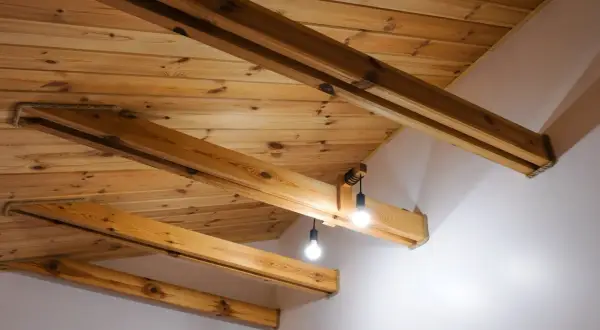 Drewniany sufit z belkami, tworzący przytulną atmosferę. Dwie lampy wiszące oświetlają przestrzeń.