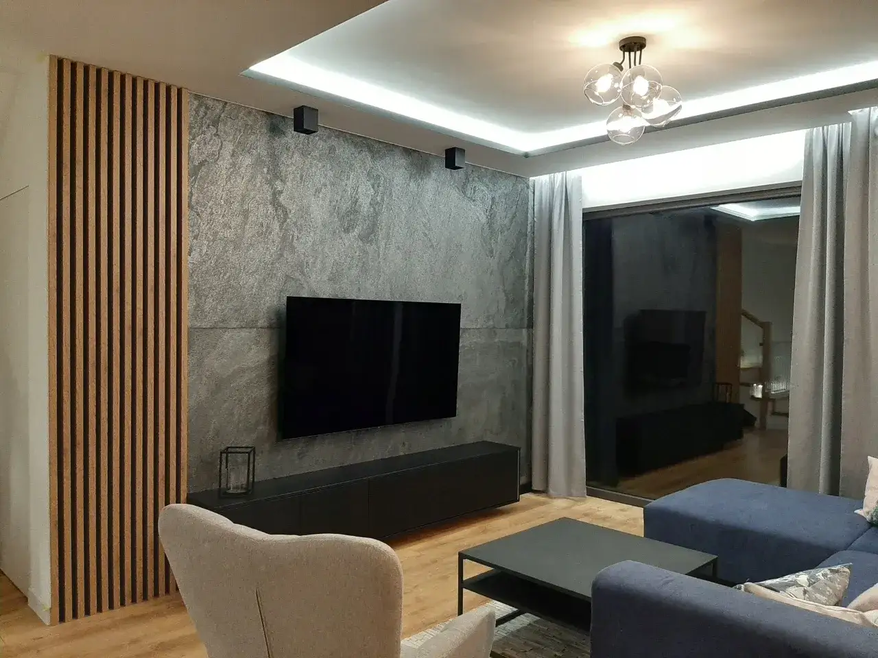 Nowoczesny salon: beton i drewno tworzą stylową przestrzeń. Drewniane lamele i betonowa ściana przyciągają wzrok.
