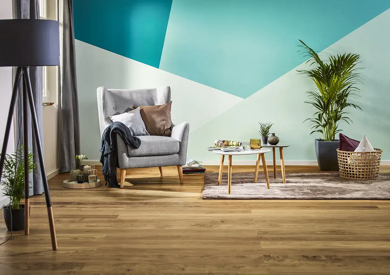 Nowoczesny salon z szarą sofą i stolikami, gdzie ściana pomalowana do połowy tworzy geometryczny wzór w odcieniach turkusu i mięty.