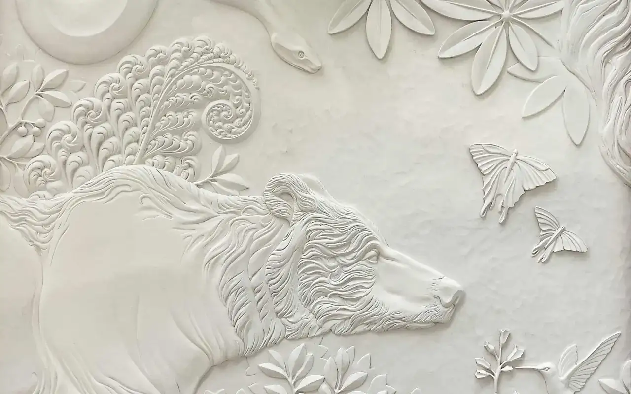 Biały, misterny relief wklęsły przedstawia niedźwiedzia, węża i motyle wśród liści.