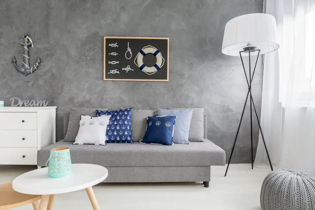 Szara ściana z kotwicą i marynistycznymi dekoracjami to świetne malowanie ścian inspiracje. Sofa z poduszkami w kotwice i muszelki.