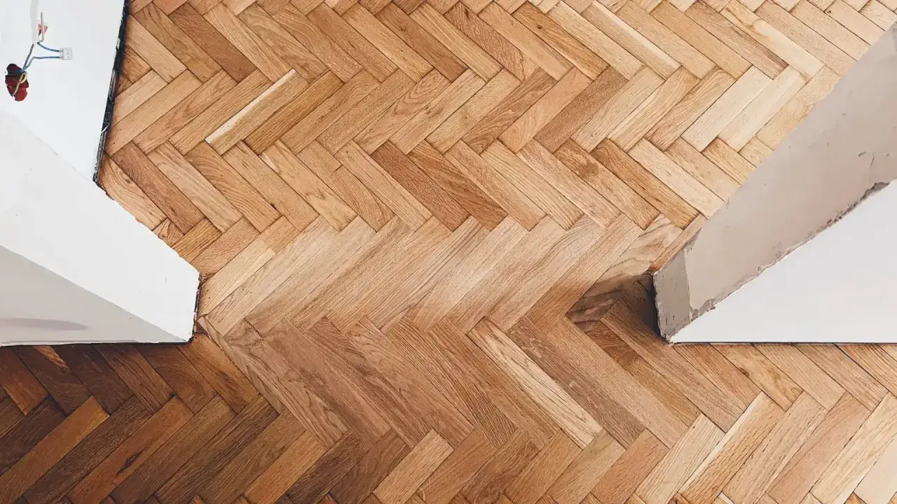 Drewniany parkiet w jodełkę, gotowy do cyklinowania parkietu samemu. Widać fragmenty ścian i instalacji elektrycznej.