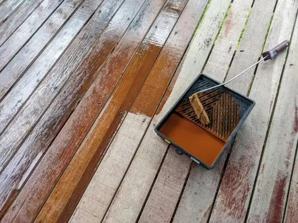 Malowanie boazerii na tarasie. Drewniane deski odzyskują blask dzięki brązowej lazurze.