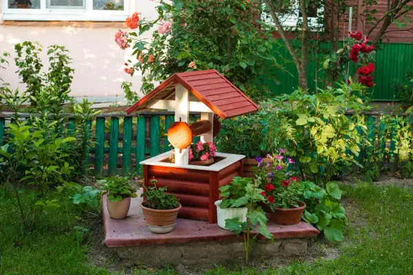 Uroczy, drewniany domek studni z ozdobnymi detalami, otoczony kwitnącymi roślinami. Ciekawe ozdoby z drewna do ogrodu dodają mu charakteru.