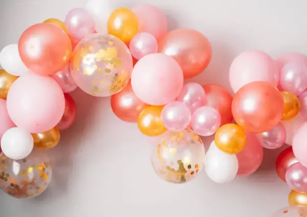 Ładna girlanda z balonów w odcieniach różu, brzoskwini i złota. Zobacz, jak zamocować balony na taśmie, by stworzyć efektowną dekorację.