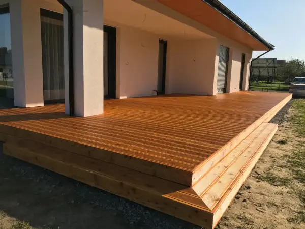 Nowa, drewniana terasa z widocznymi stopniami, zabezpieczona impregnatem do legarów tarasowych, lśni w słońcu.