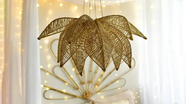 Złota lampa z koralików diy w kształcie liścia, wisząca na tle białych zasłon i migoczących światełek.