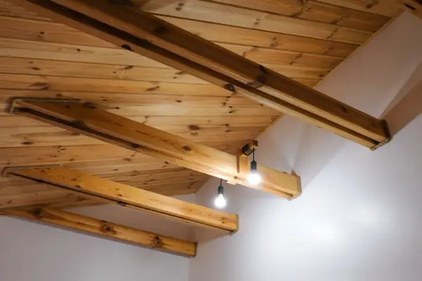 Drewniany sufit z belkami, tworzący przytulną atmosferę. Dwie lampy wiszące oświetlają przestrzeń.